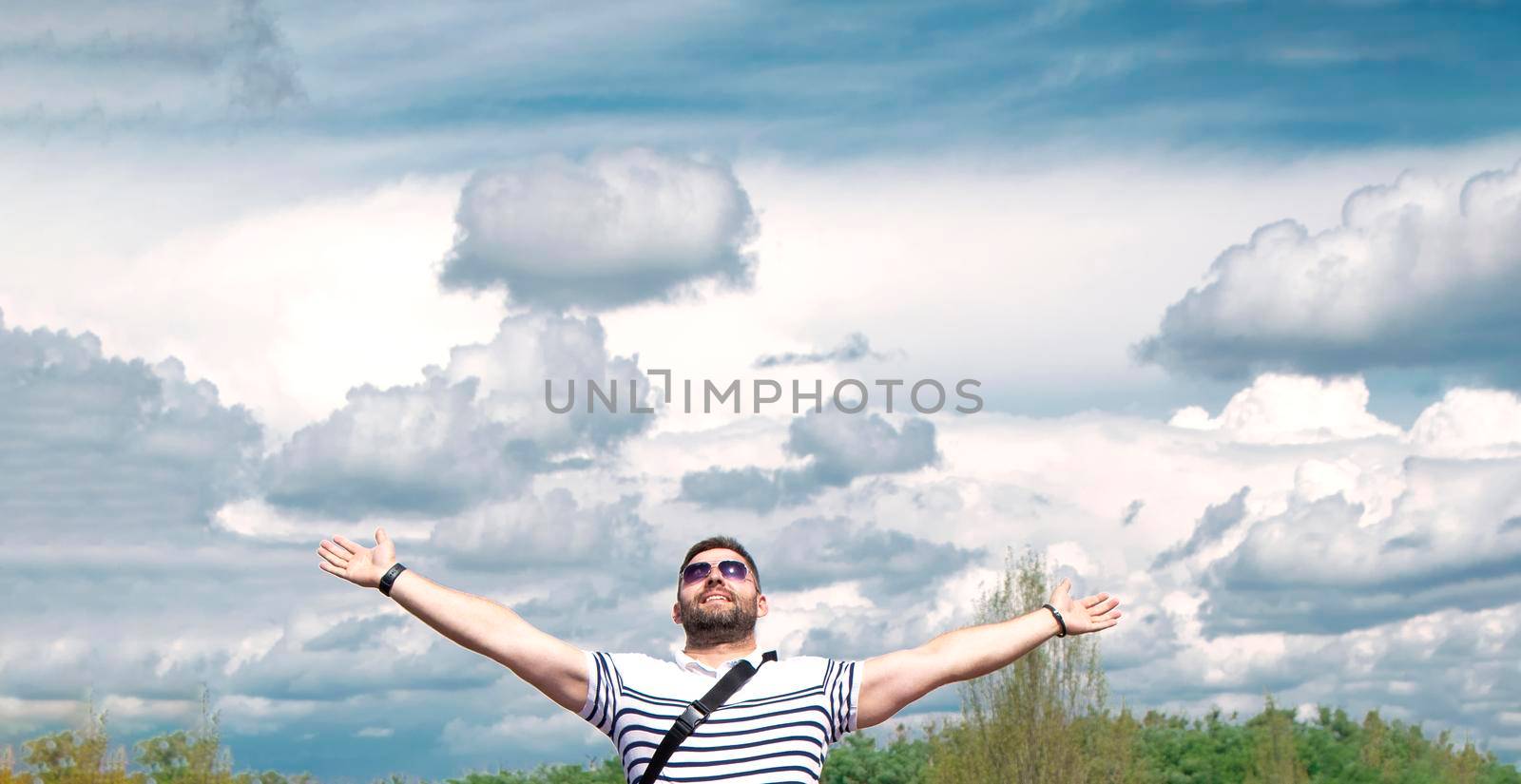 man raised his hands up against the background of the sky with clouds. Smiling, happy. The concept of gratitude and success. Place for text. High quality photo