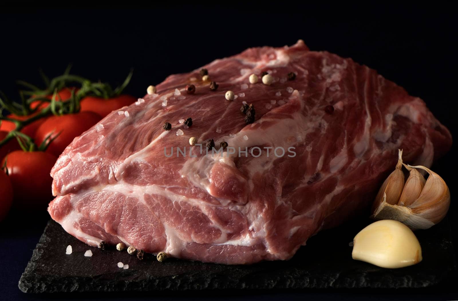 Raw pig meat on a black background. Ingredients for roasting pork, tomatoes and pork. Fresh pork tenderloin. a large piece of loin. Seasoned meat with pepper and salt . Ready to cook