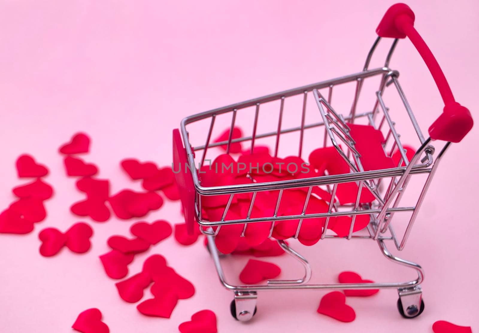 Selective focus. shopping cart filled with red hearts on a pink background. Decorative basket with small hearts. The concept of gifts to a loved one, love. High quality photo