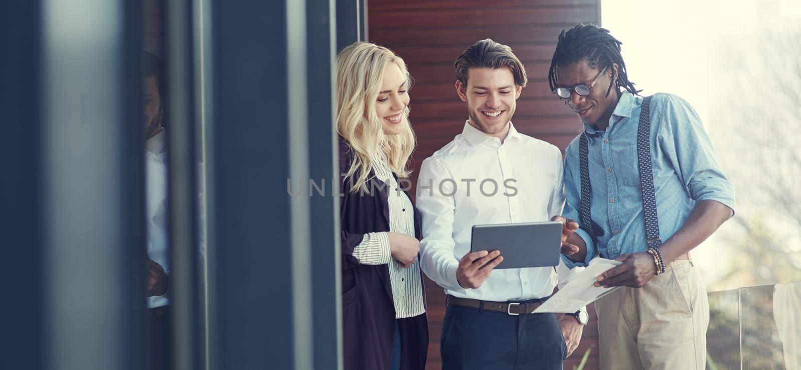 Doing business on the balcony. Cropped shot of three young businesspeople using a tablet while standing outside on the office balcony. by YuriArcurs