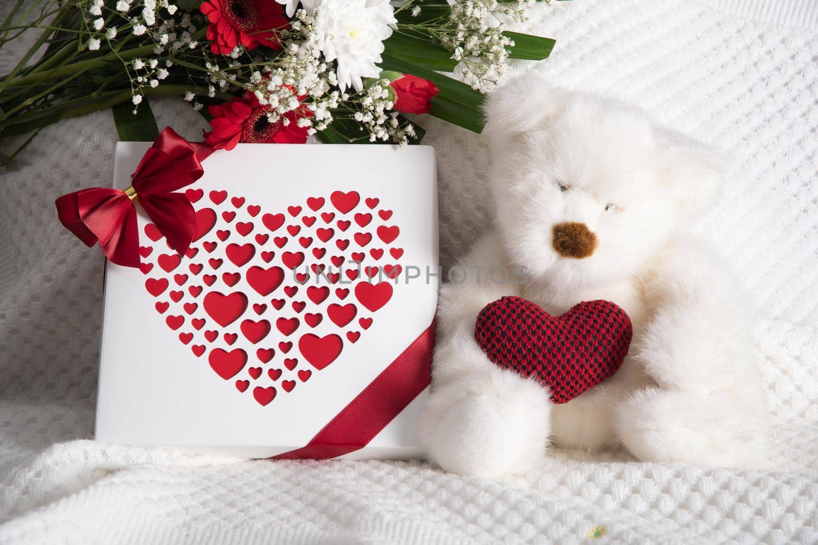 Valentine's day gift, teddy bear with a heart, a box of pralines and a bouquet of flowers on the bed early in the morning. High quality photo