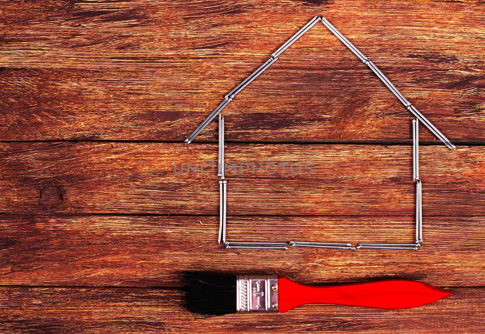 This is an overhead photo of nails in the shape of a home building and brush. There is a lot of space for copy inside the house shape.