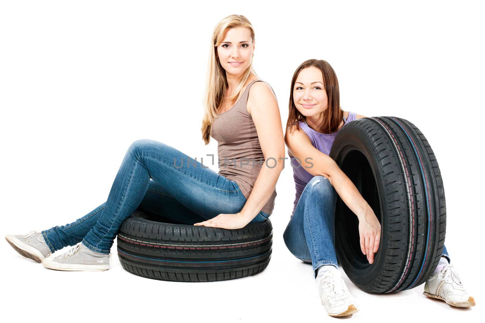 Two young girls sitting on the car wheels, isolated on white.