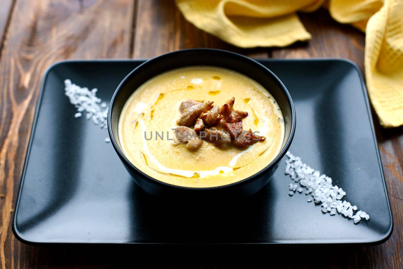 Pumpkin vegetable cream soup on black bowl with pork or chicken meat. Wooden background