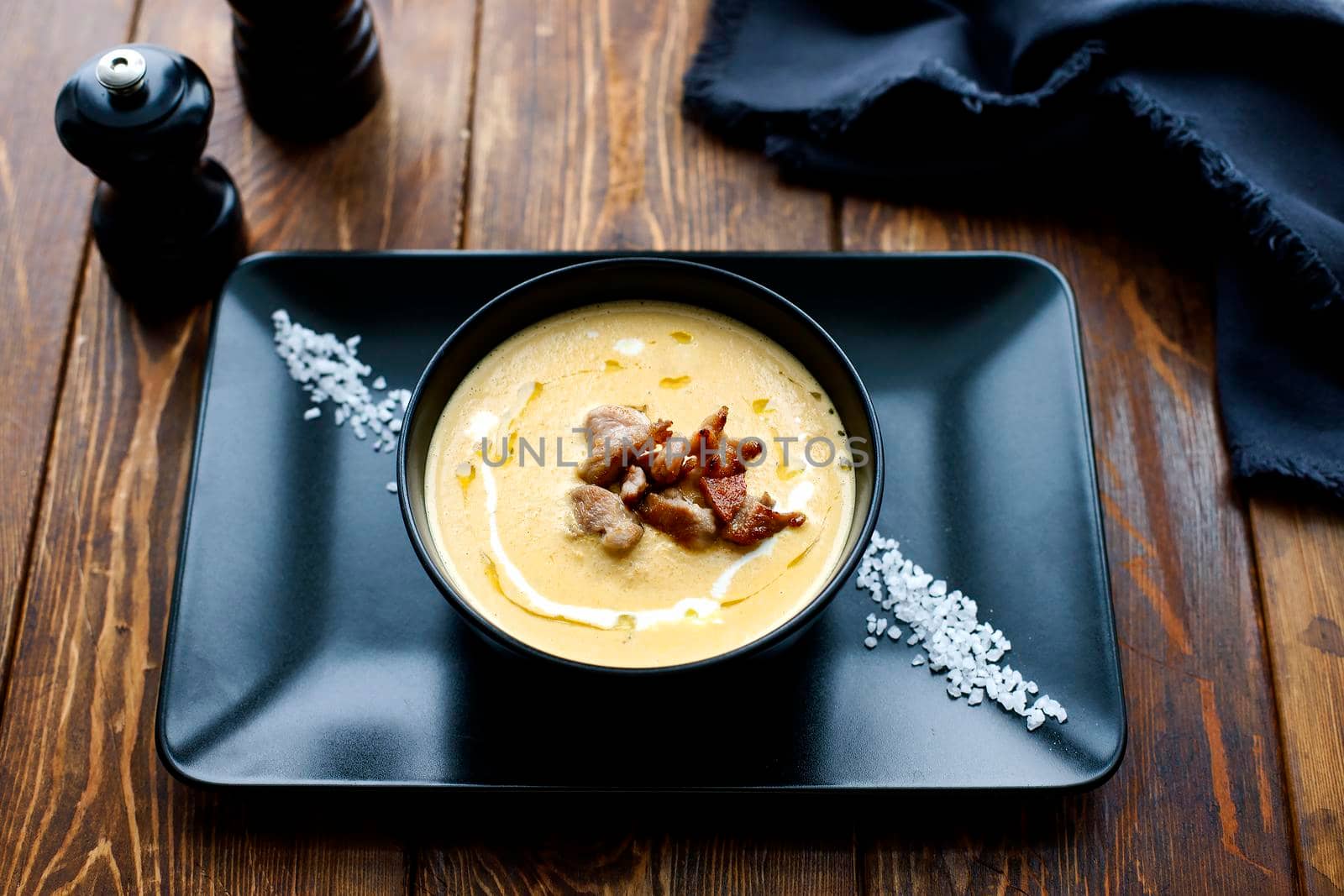 Pumpkin vegetable cream soup on black bowl with pork or chicken meat. Wooden background