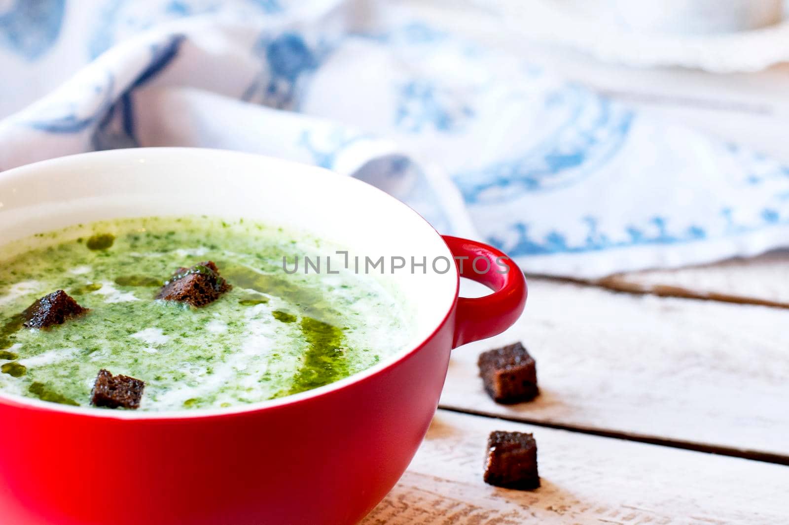 Spinach soup with croutons in red bowl on wooden table