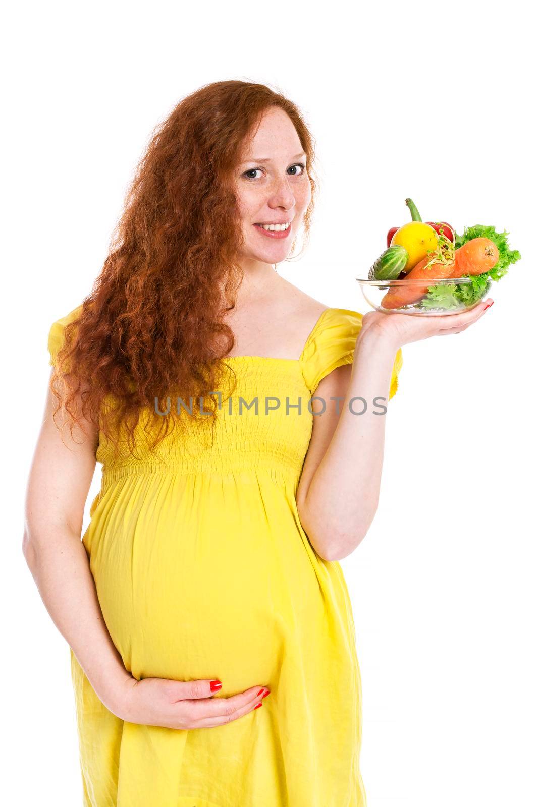 Pregnant woman holding a bowl of vegetables and smiling. Isolated on white.