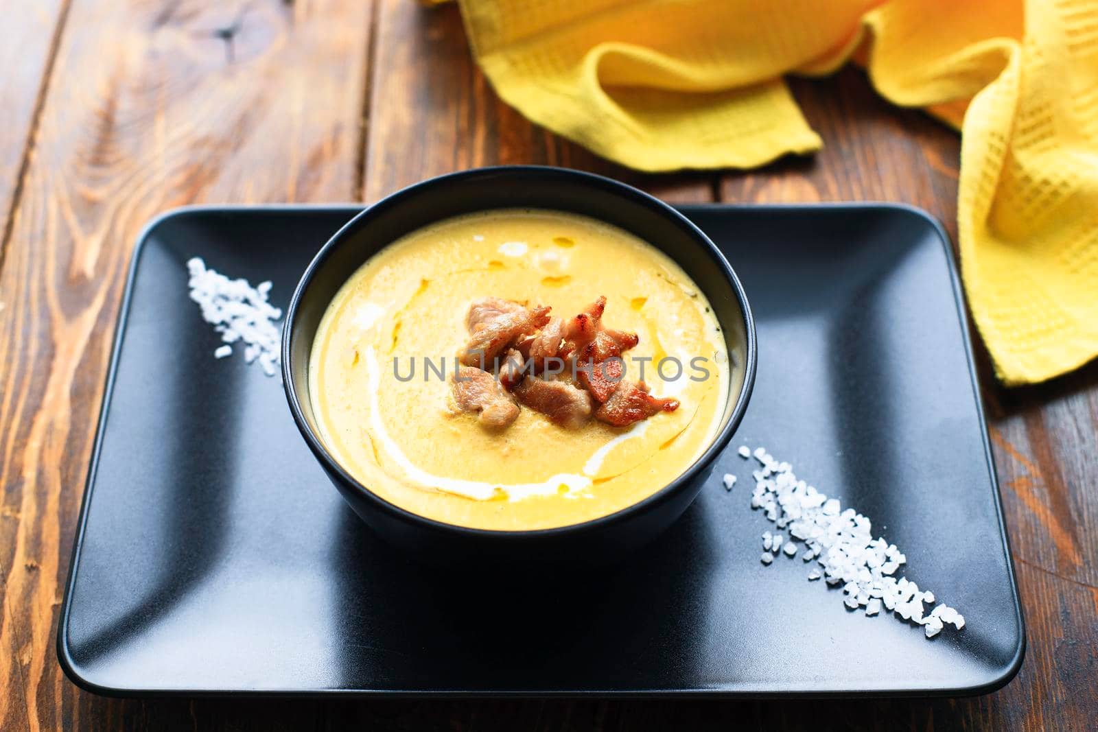 Pumpkin vegetable cream soup on black bowl with pork or chicken meat. Wooden background