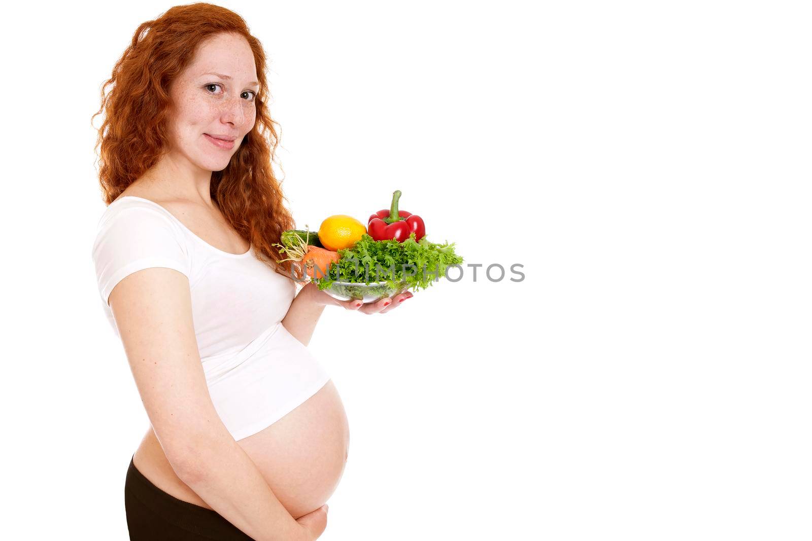 Pregnant woman holding a bowl of vegetables and smiling. Isolated on white.