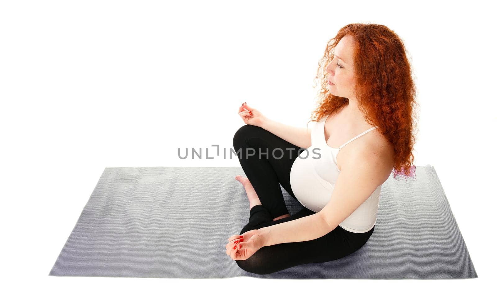 Pregnant woman sitting cross-legged and doing yoga. Isolated on white.