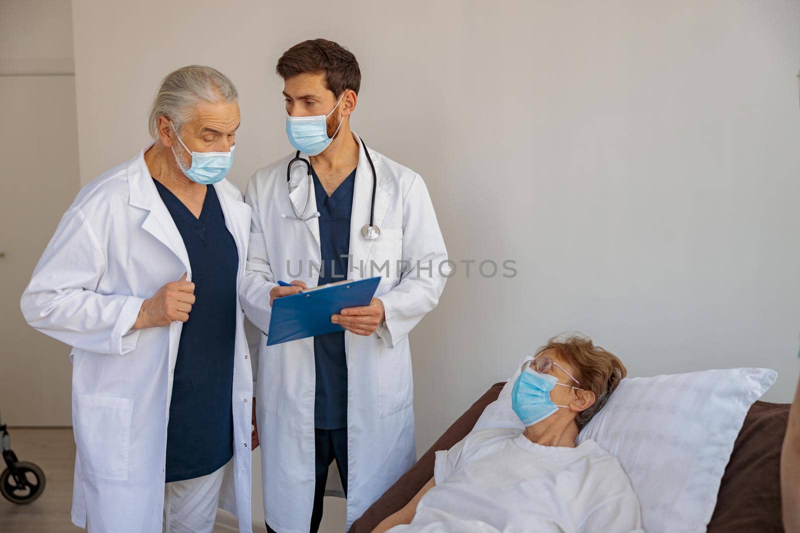 Professional doctors in mask discuss over patient's diagnosis standing in hospital ward by Yaroslav_astakhov