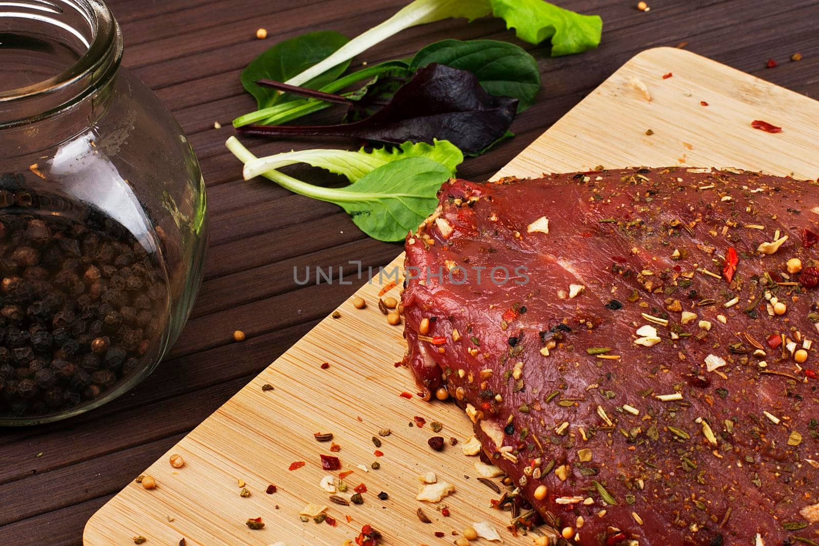Raw Beef Roast with Fresh Herbs on a dark wooden table.