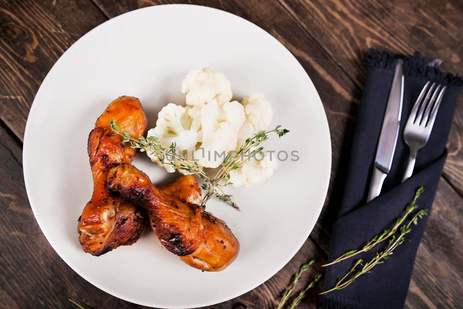 Baked chicken drumsticks with cauliflower served on a wooden table. Rustic style. Top view