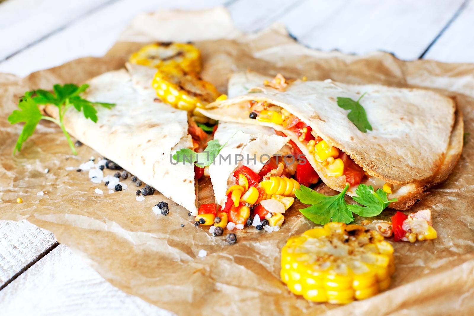 Mexican Quesadilla wrap with vegetables, corn, sweet pepper and sauces on the parchment and table. horizontal view.