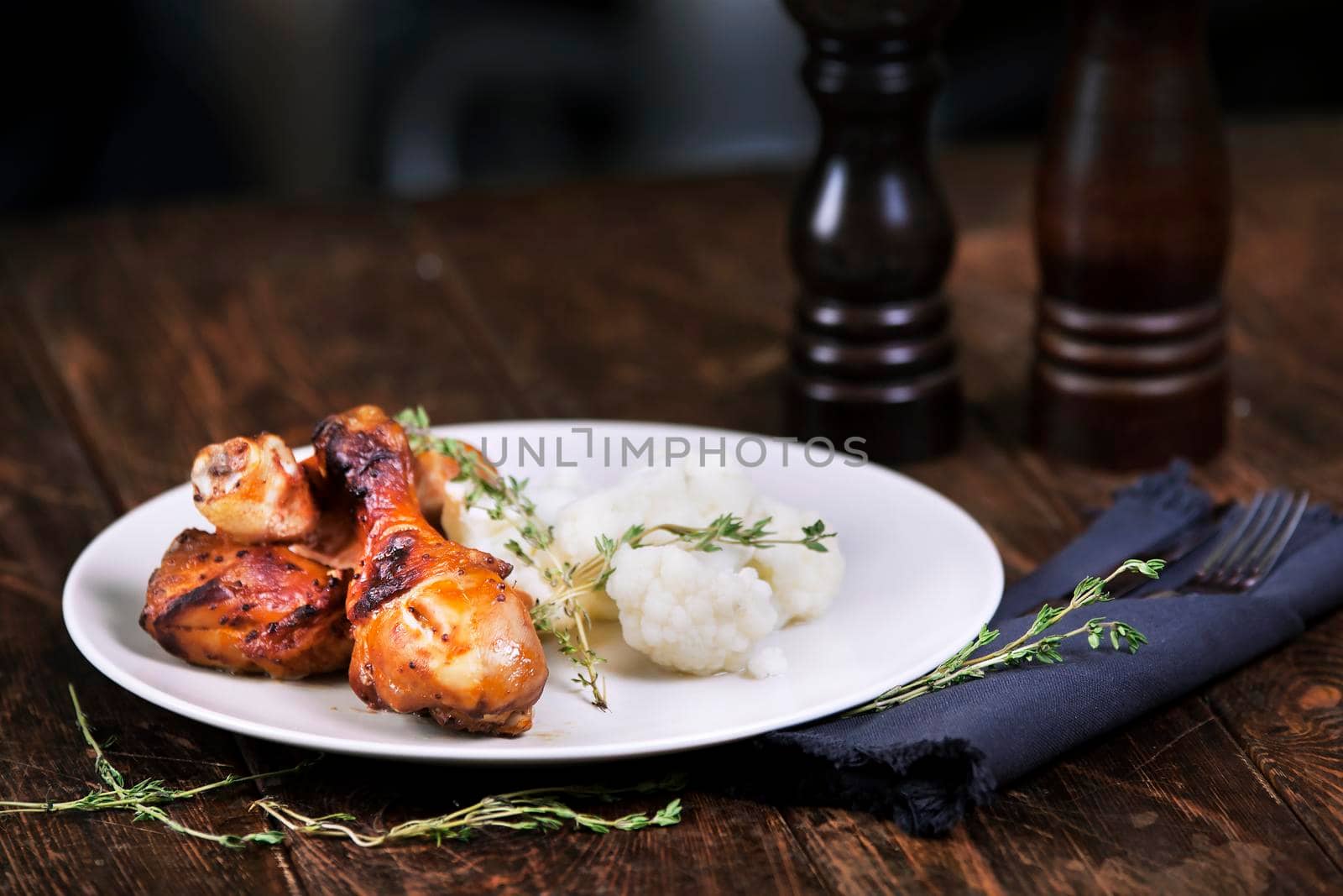 Baked chicken drumsticks with cauliflower served on a wooden table. Rustic style