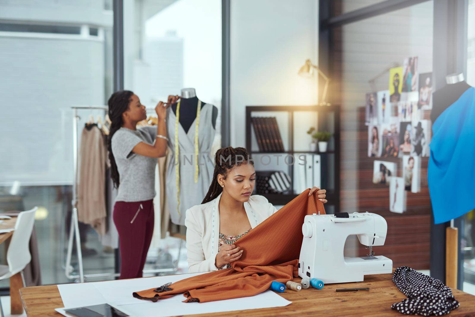 Shot of a young fashion designer sewing garments while a colleague works on a mannequin in the background.