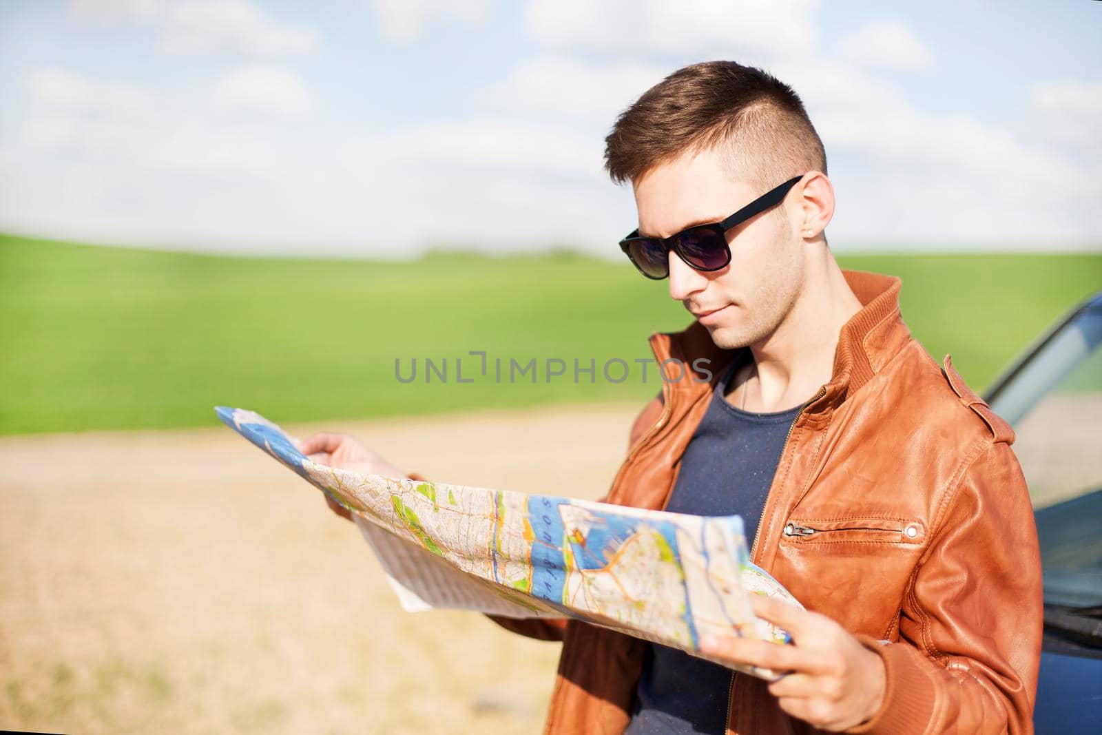 Photo of a traveler parked his car by the side of a road, lost and reading the map. Focus on the map and male.
