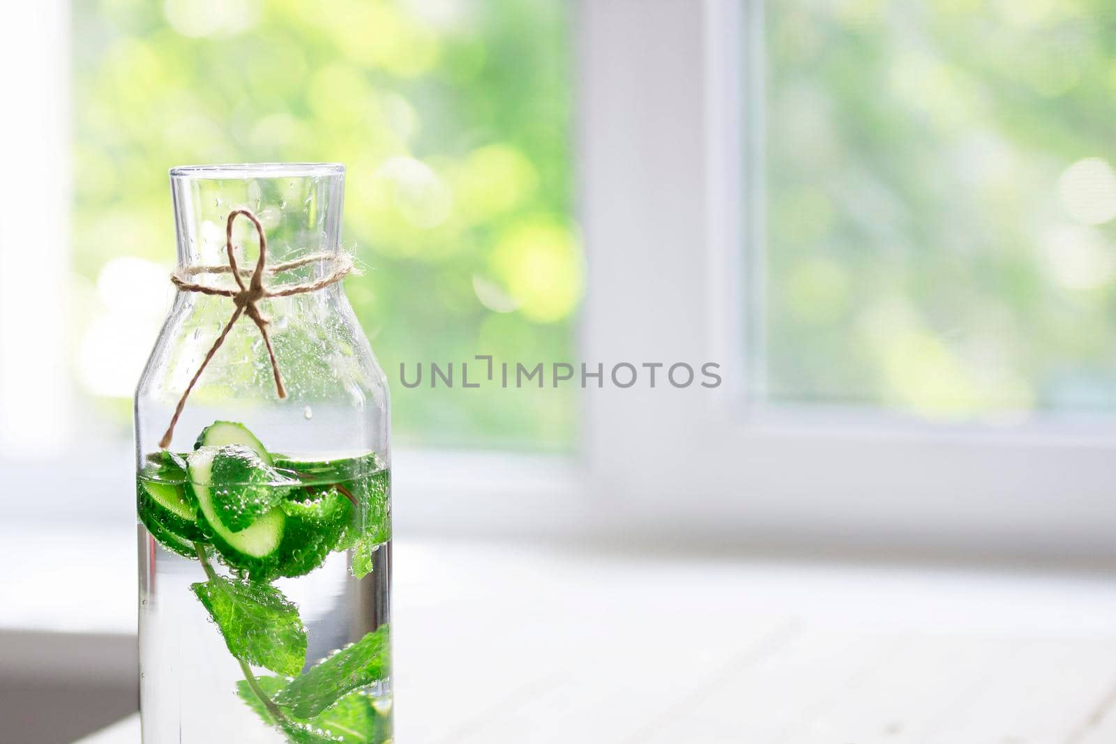 Nutritious detox water or emonade with cucumber and mint on table near window. Copy space for text.