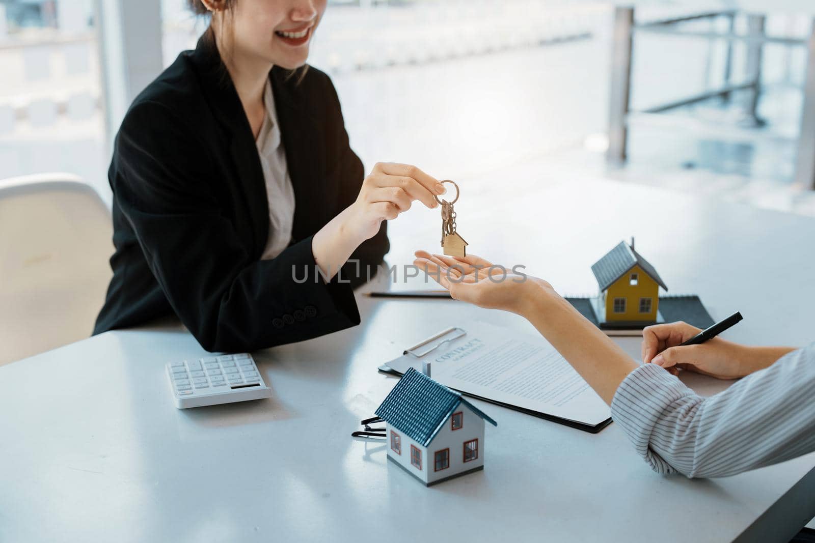 Accountant, businessman, real estate agent, Asian business woman handing keys to customers along with house after customers to sign.