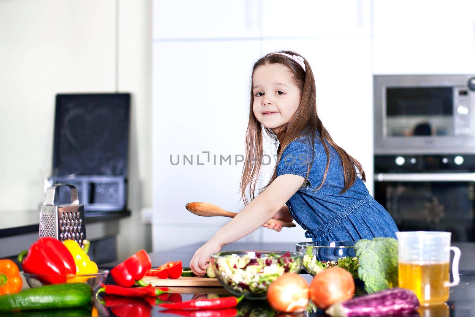 little daughter cooking in the kitchen at home. Girl Assisting In Preparing Food - Stock image