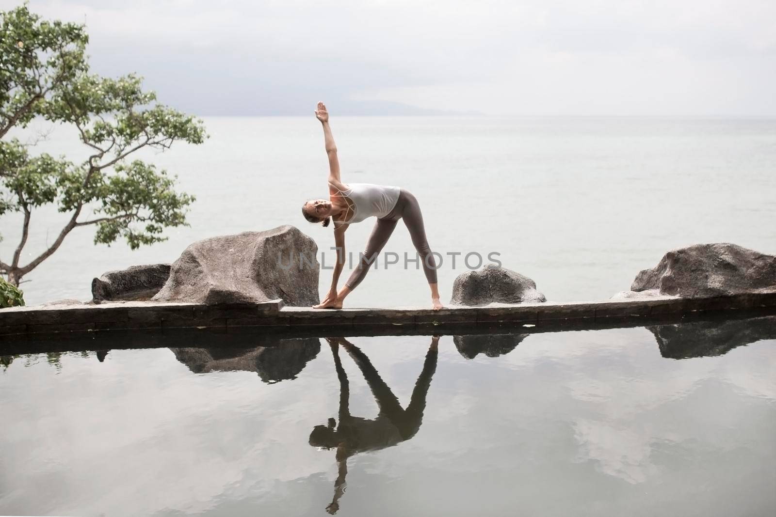 The silhouette of a beautiful young woman practicing yoga in front of the lake at sunrise.