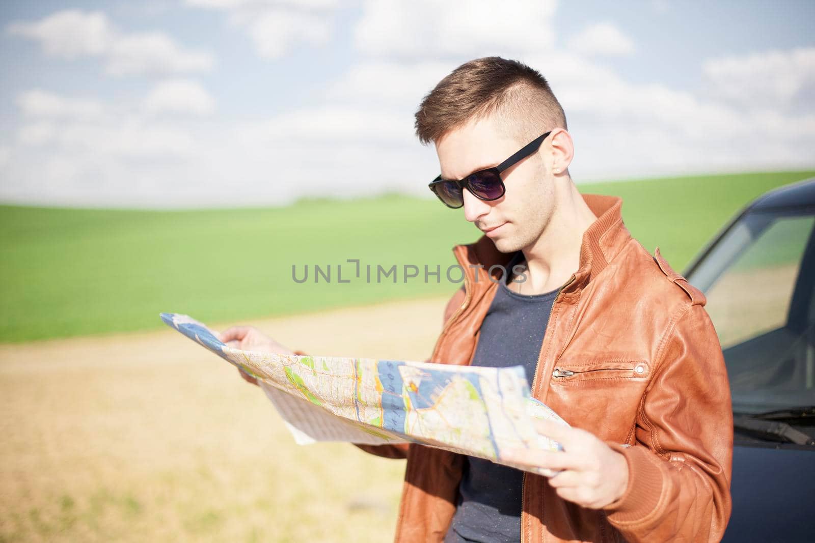 A tourist man next to the car looks at the map of the area for further travel.