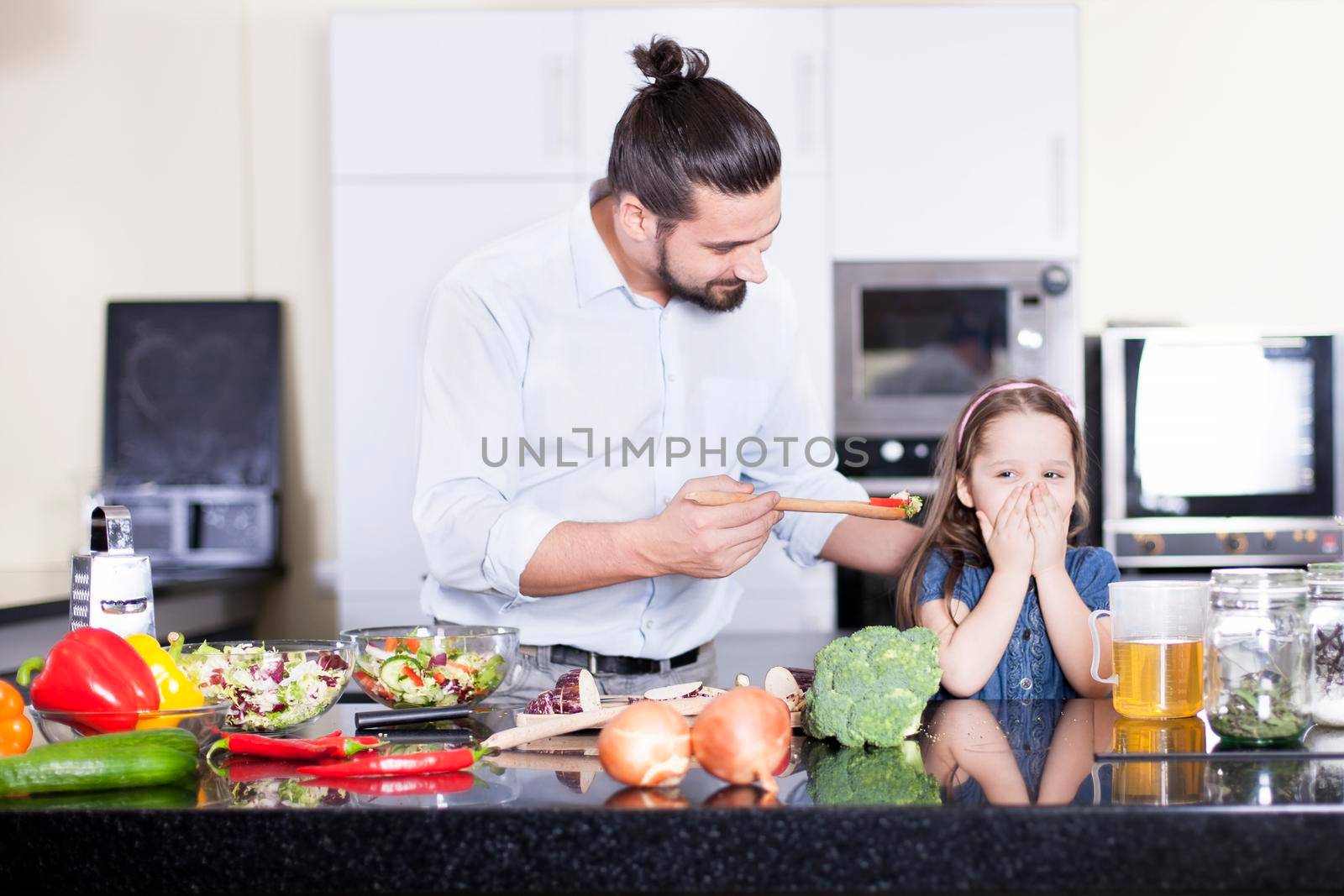 Little girl refusing to eat a salad while cooking and having lunch together in the kitchen by Jyliana