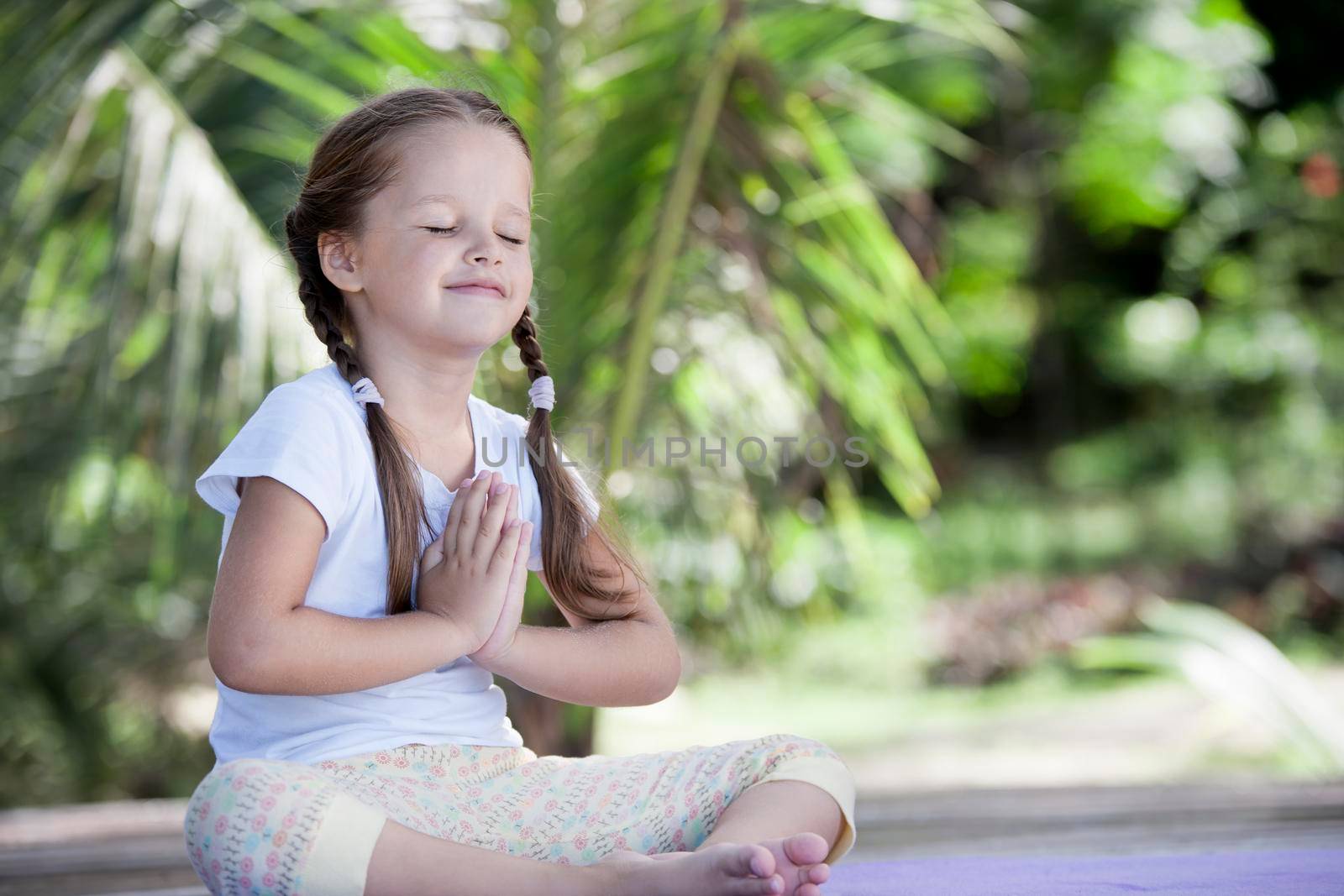 Child doing exercise on platform outdoors. Healthy ocean lifestyle. Yoga girl