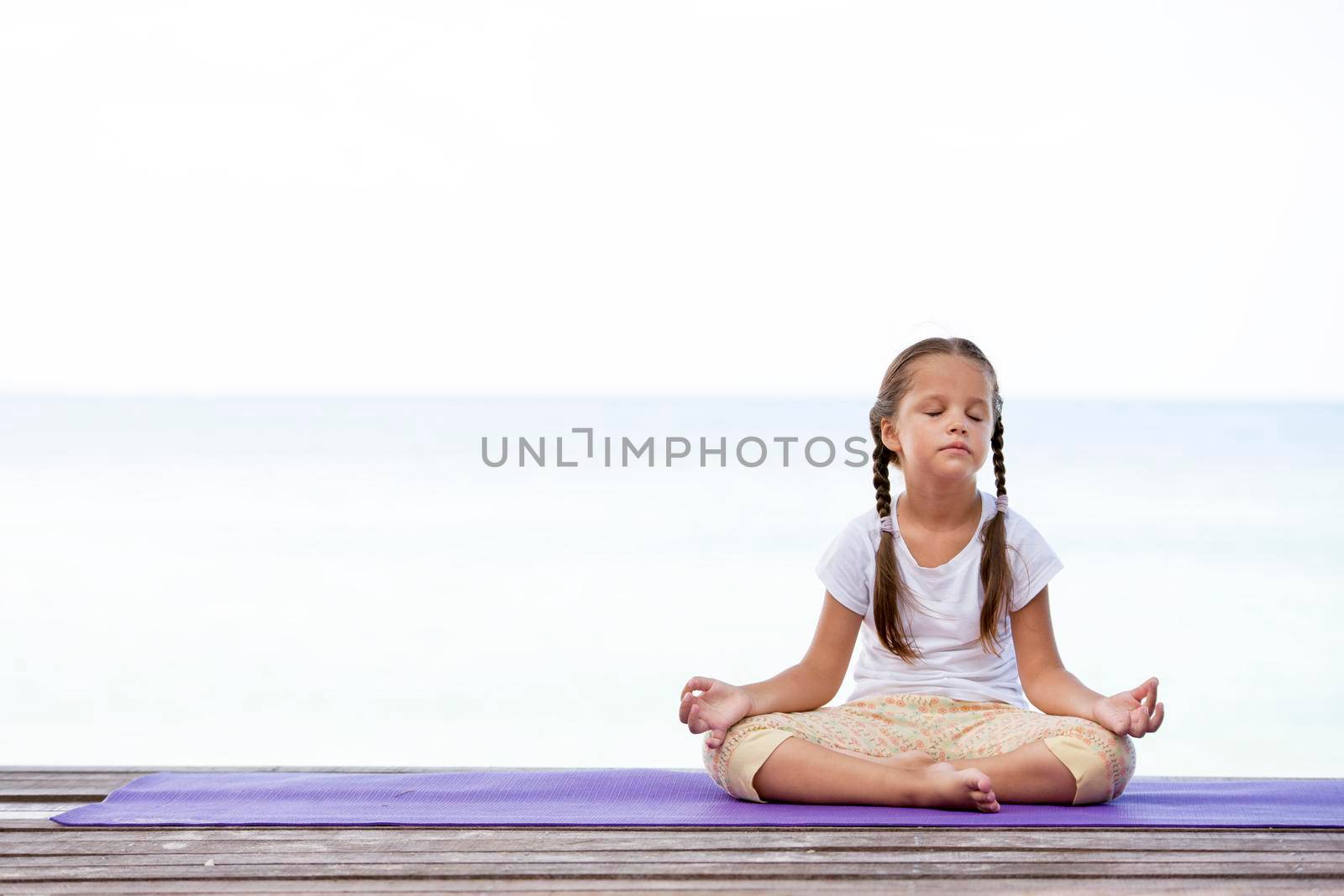 Child doing exercise on platform outdoors. Healthy ocean lifestyle. Yoga girl