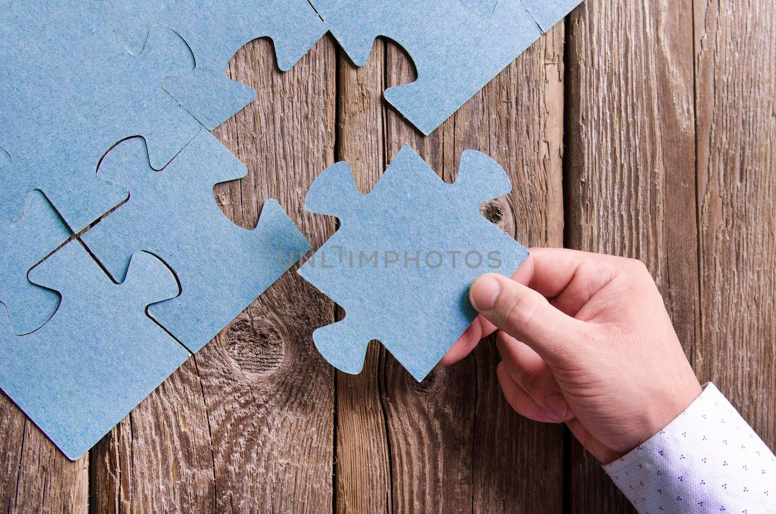 Incomplete puzzles lying on wooden rustic boards. Conceptual of innovation, solution finding and integration. Hand with puzzle piece