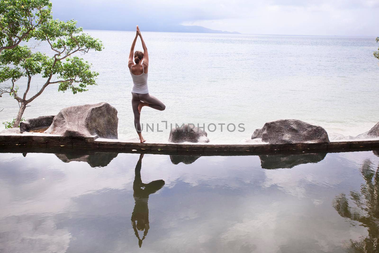 The silhouette of a beautiful young woman practicing yoga in front of the lake at sunrise.