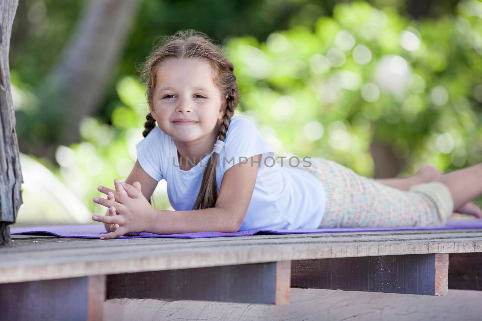 Child doing exercise on platform outdoors. Healthy lifestyle. Yoga girl by Jyliana