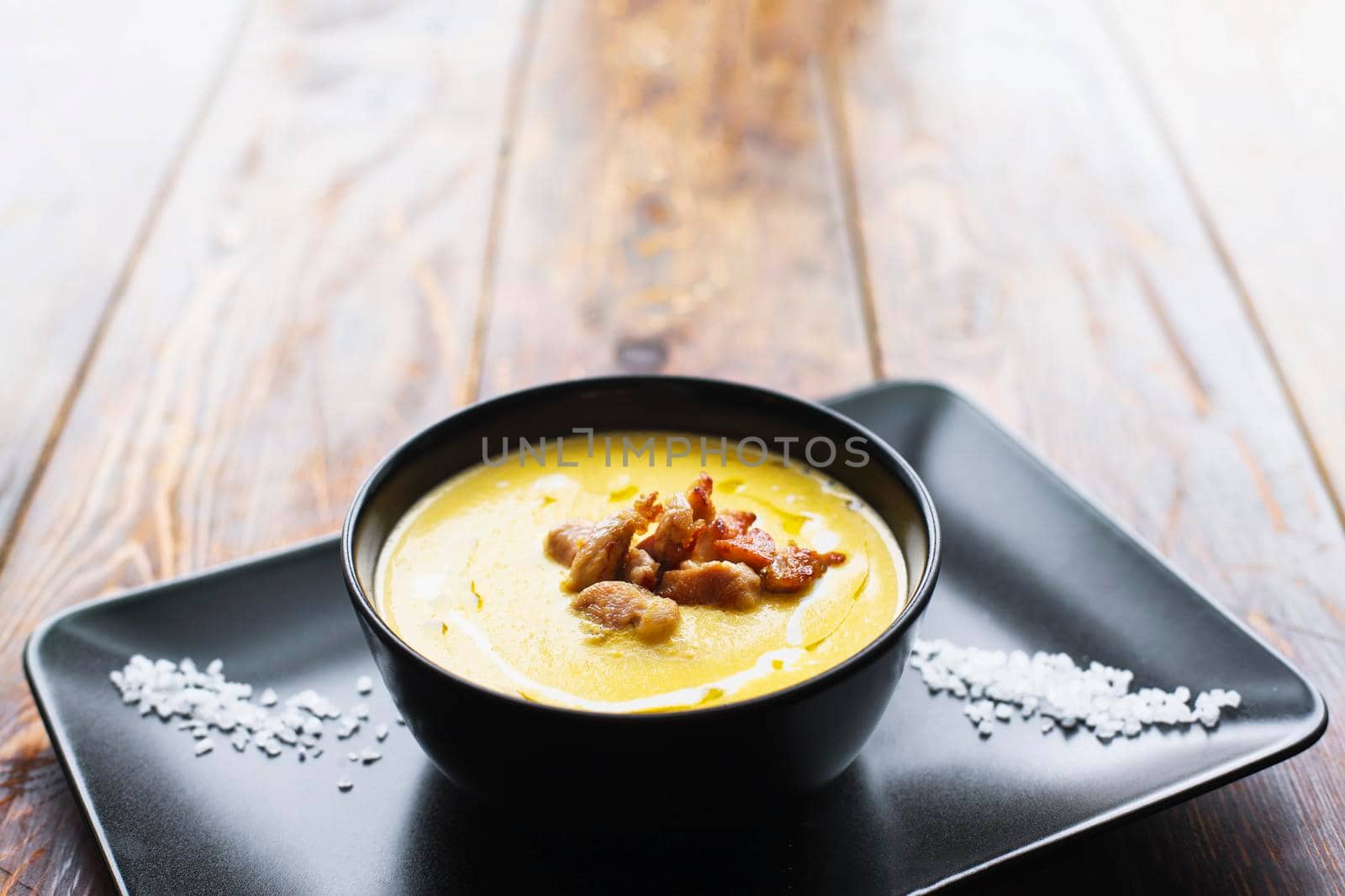 Pumpkin vegetable cream soup on black bowl with pork or chicken meat. Wooden background