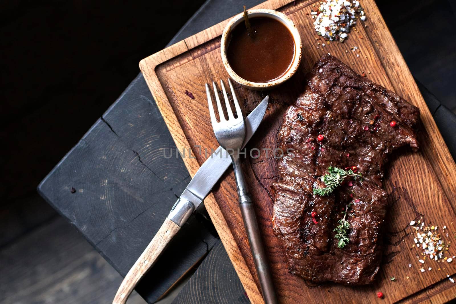 Beefsteak. Piece of grilled BBQ beef marinated in spices and herbs on rustic wooden board over rough wooden desk with copy space. Top view.