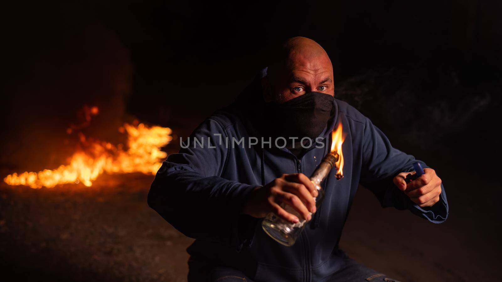 A masked man is holding a burning bottle. Molotov cocktail