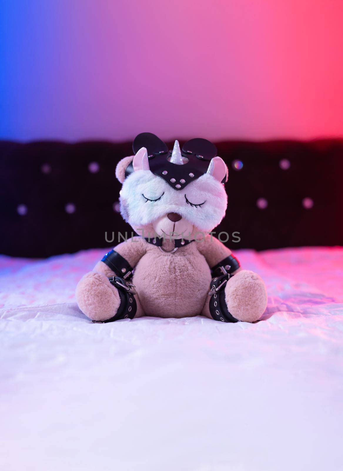 the toy teddy bear dressed in leather straps and a mask, an accessory for BDSM games in a sleep mask