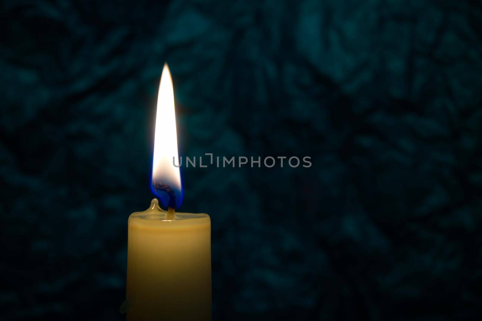 Single yellow wax candle burning alone in the dark background. Conceptual image symbolize peace, love, hope or patience with free copy space