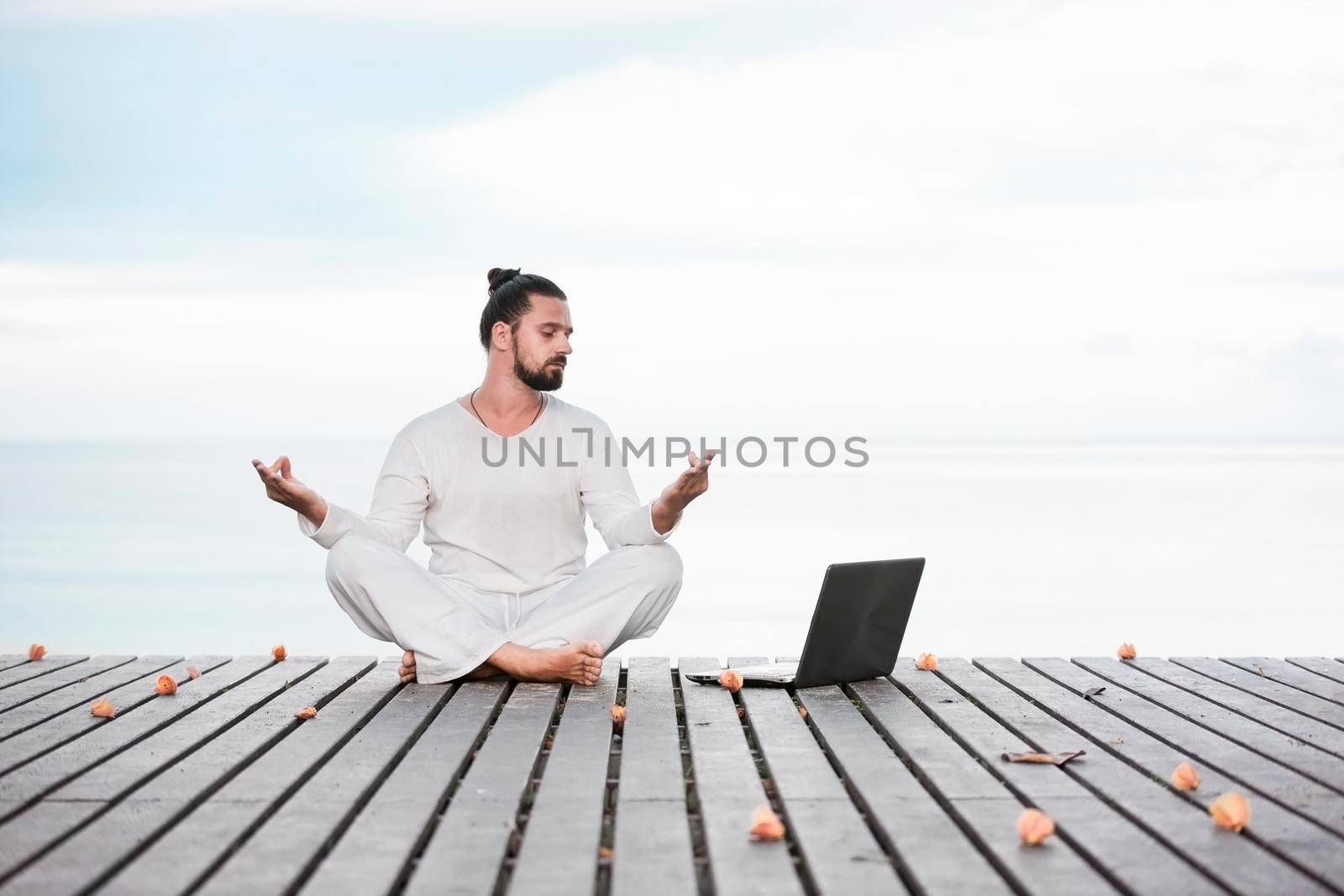 Man in white clothes meditating yoga on wooden pier by Jyliana