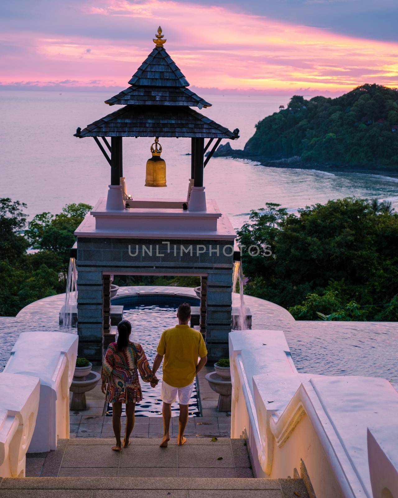 a young couple of men and women at a swimming pool during a vacation on a tropical island. man and woman in infinity pool during sunset. luxury vacation in Thailand pool of a luxury pool villa