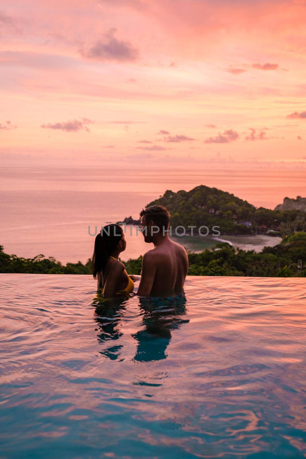 young couple men and women at the swimming pool during vacation at the tropical islandscouple man and woman in infinity pool during sunset by fokkebok