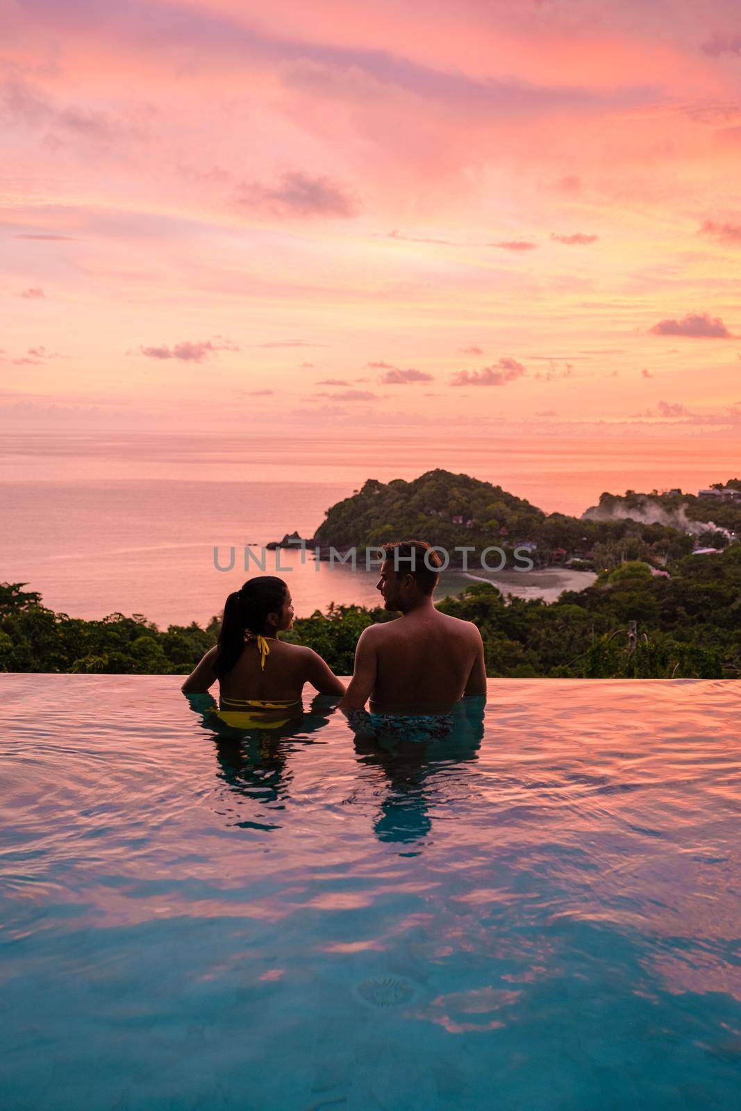 a young couple of men and women at a swimming pool during a vacation on a tropical island. man and woman in infinity pool during sunset. luxury vacation in Thailand pool of a luxury pool villa