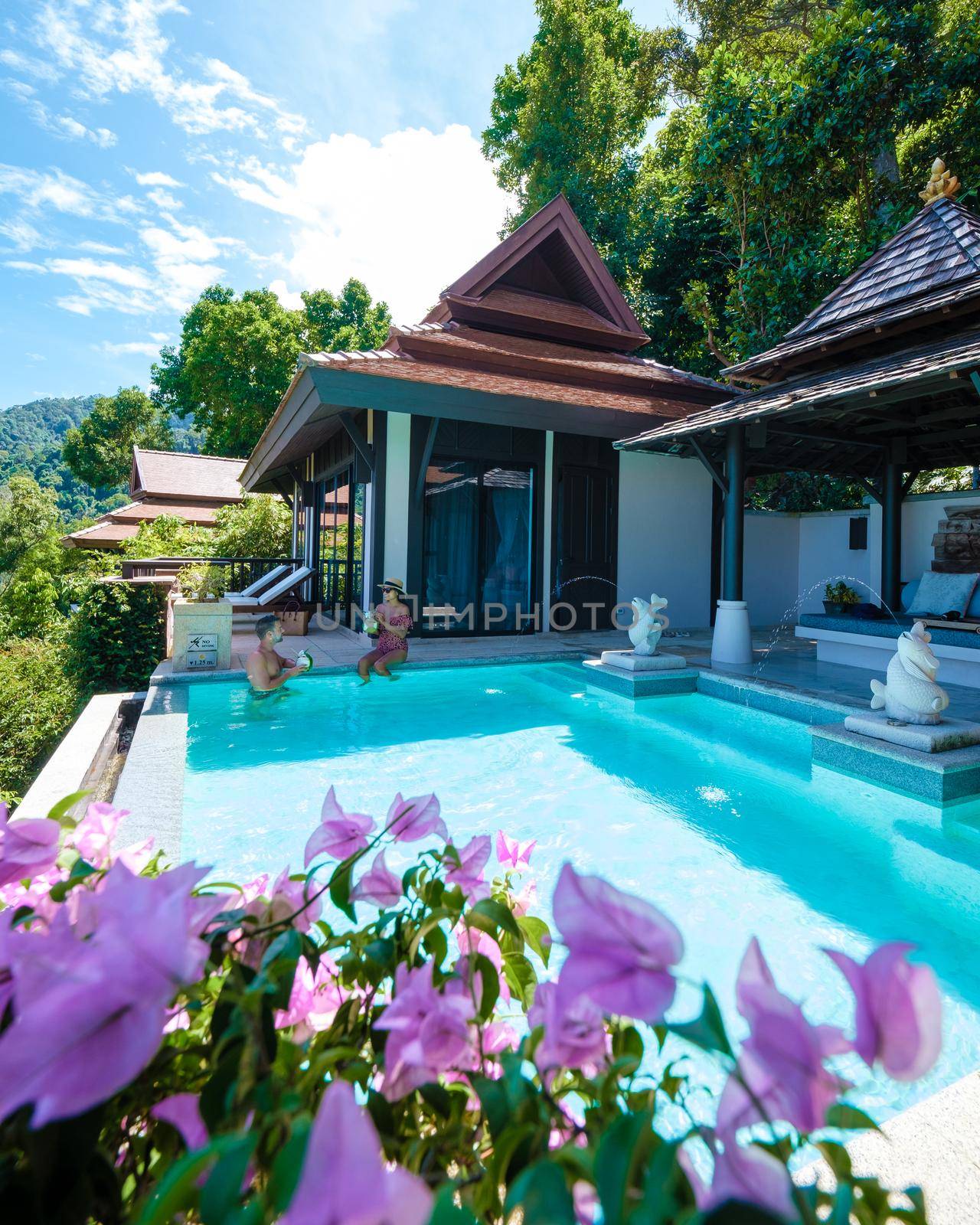 a young couple of men and women at a swimming pool during a vacation on a tropical island. man and woman in infinity pool during sunset. luxury vacation in Thailand pool of a luxury pool villa