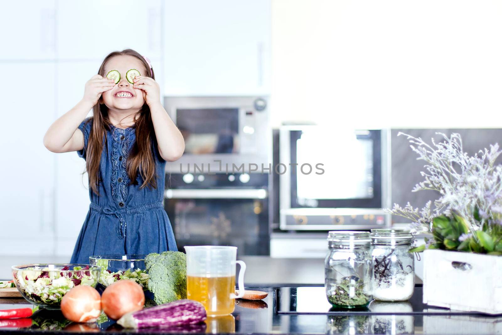 little daughter cooking in the kitchen at home. Girl Assisting In Preparing Food - Stock image