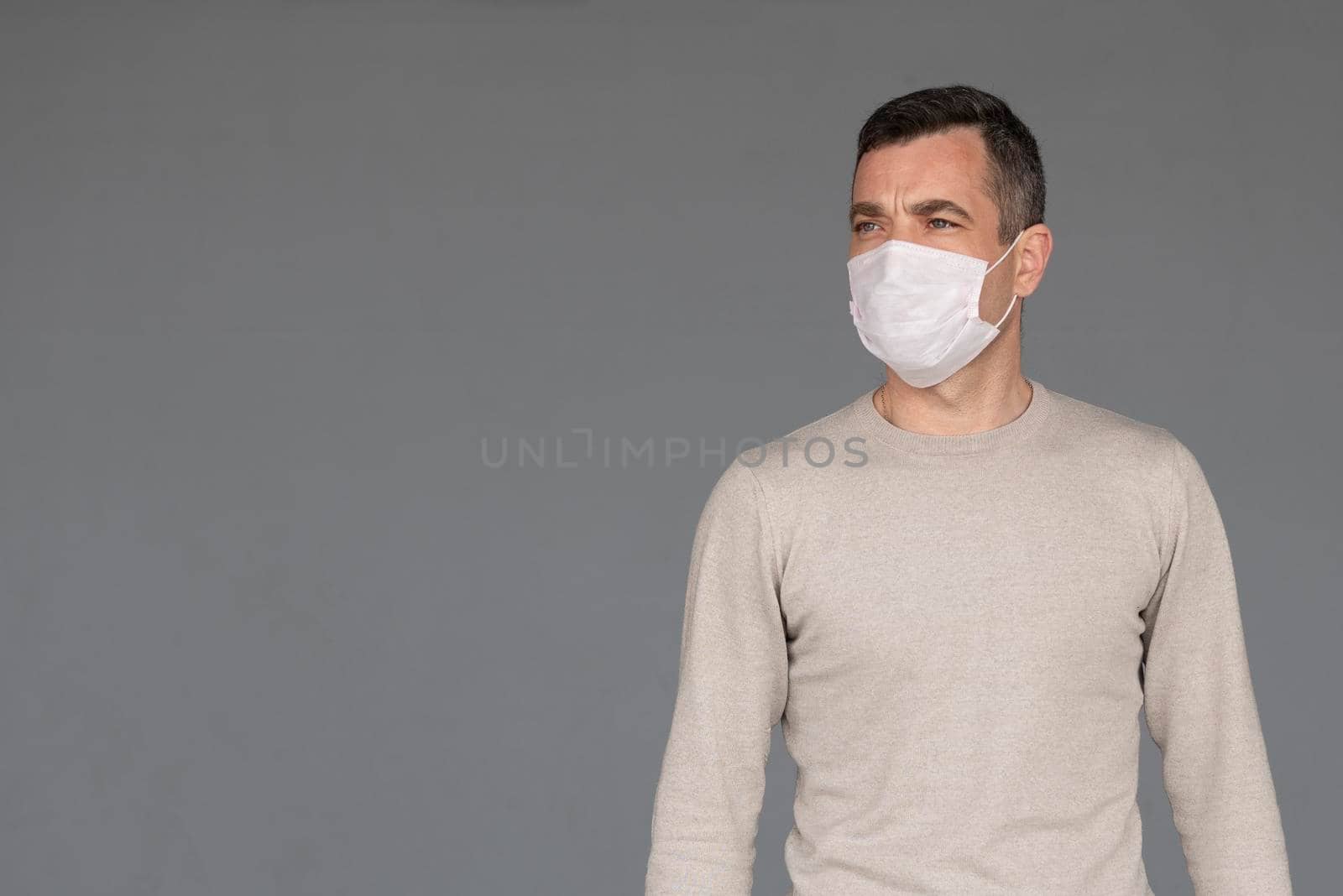 Young man wearing surgical white face mask and black gloves isolated on grey background with copy space