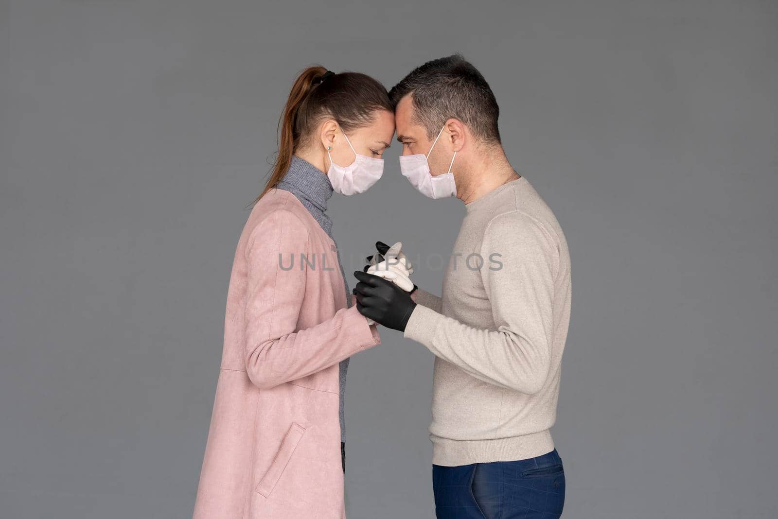 happy couple in love in repsiratory masks and gloves hugging each other isolated on grey by Jyliana