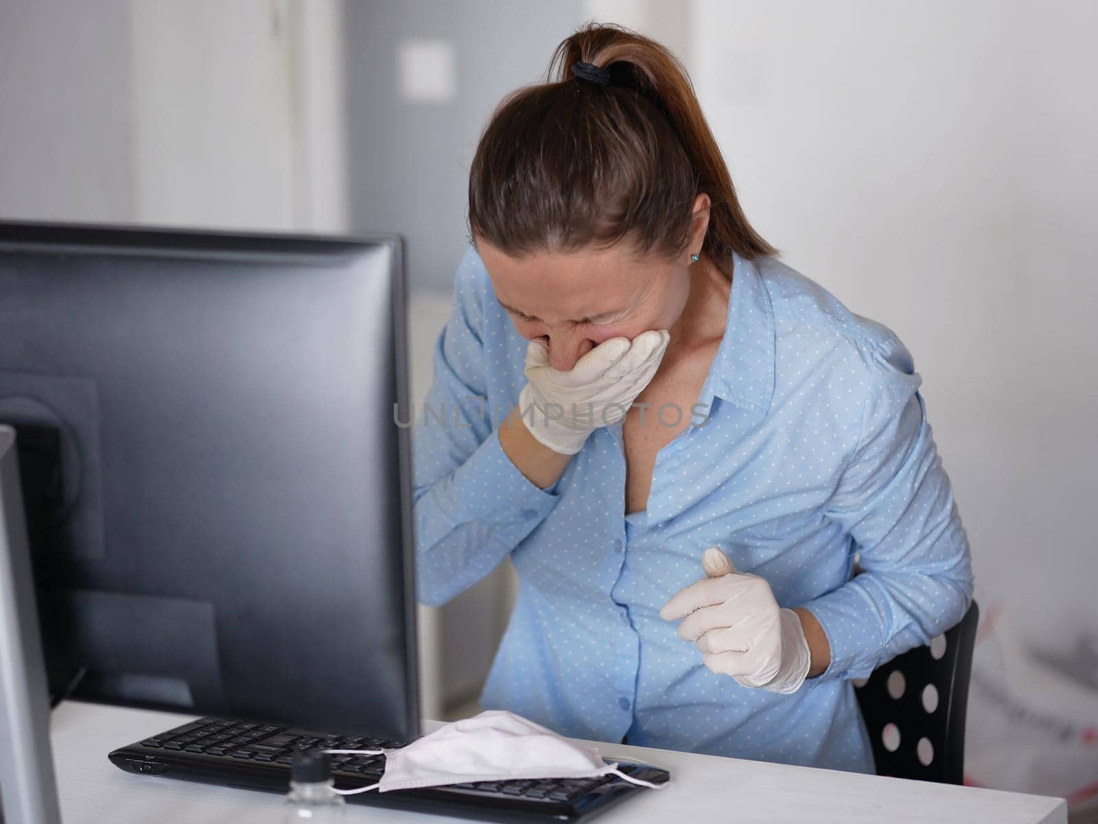 Ill young woman using laptop wearing face mask and coughing, working from home or at office, close up by Jyliana