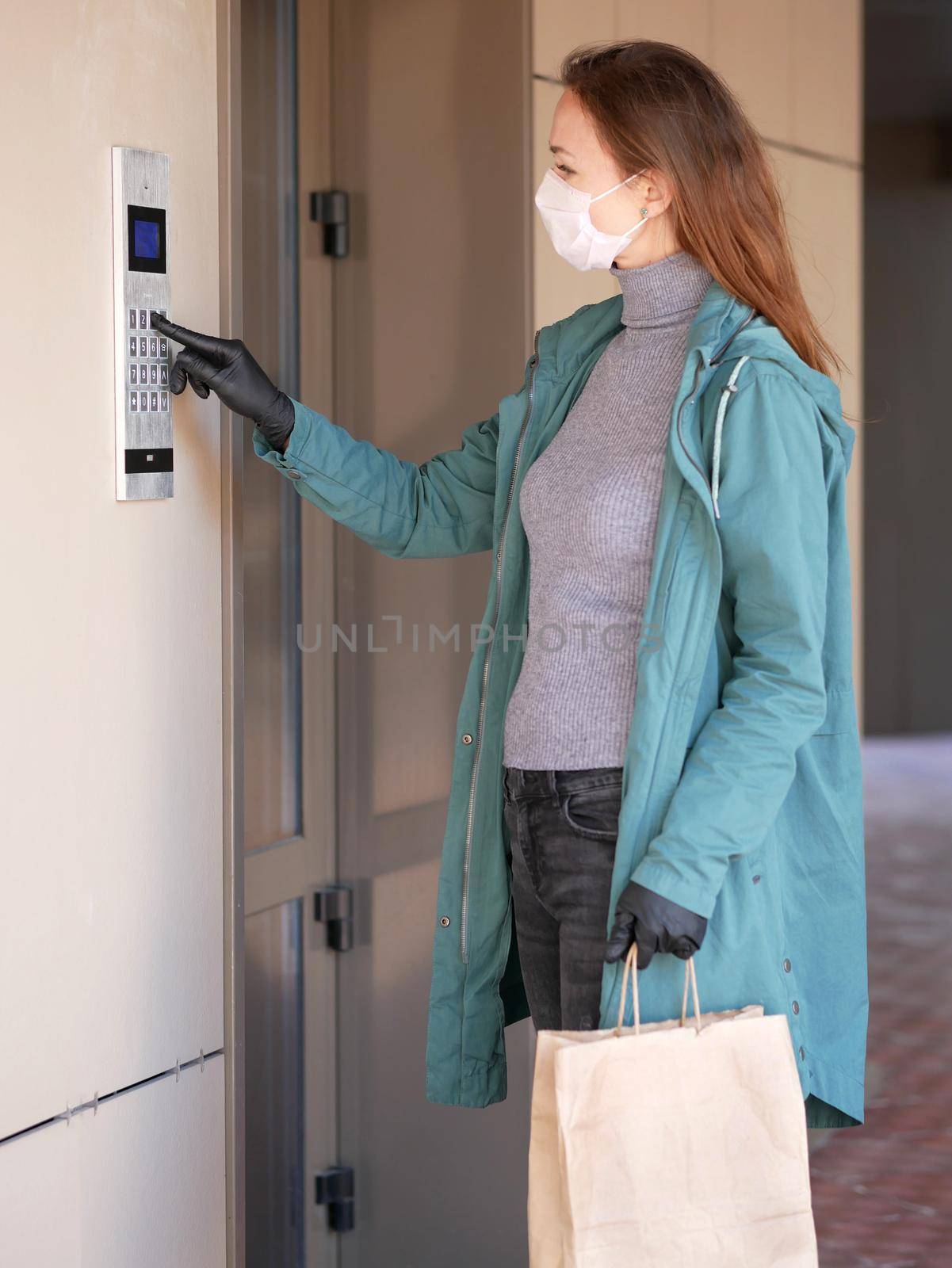 Woman wearing a mask for prevent virus with shopping bags dials the door code by Jyliana