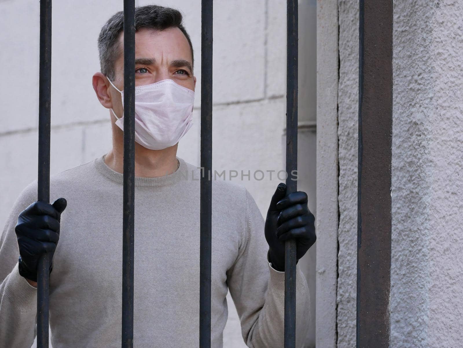 A man in white protective face mask near metal fence. Quarantine. Coronavirus concept. A man wearing protective mask. Pandemic covid