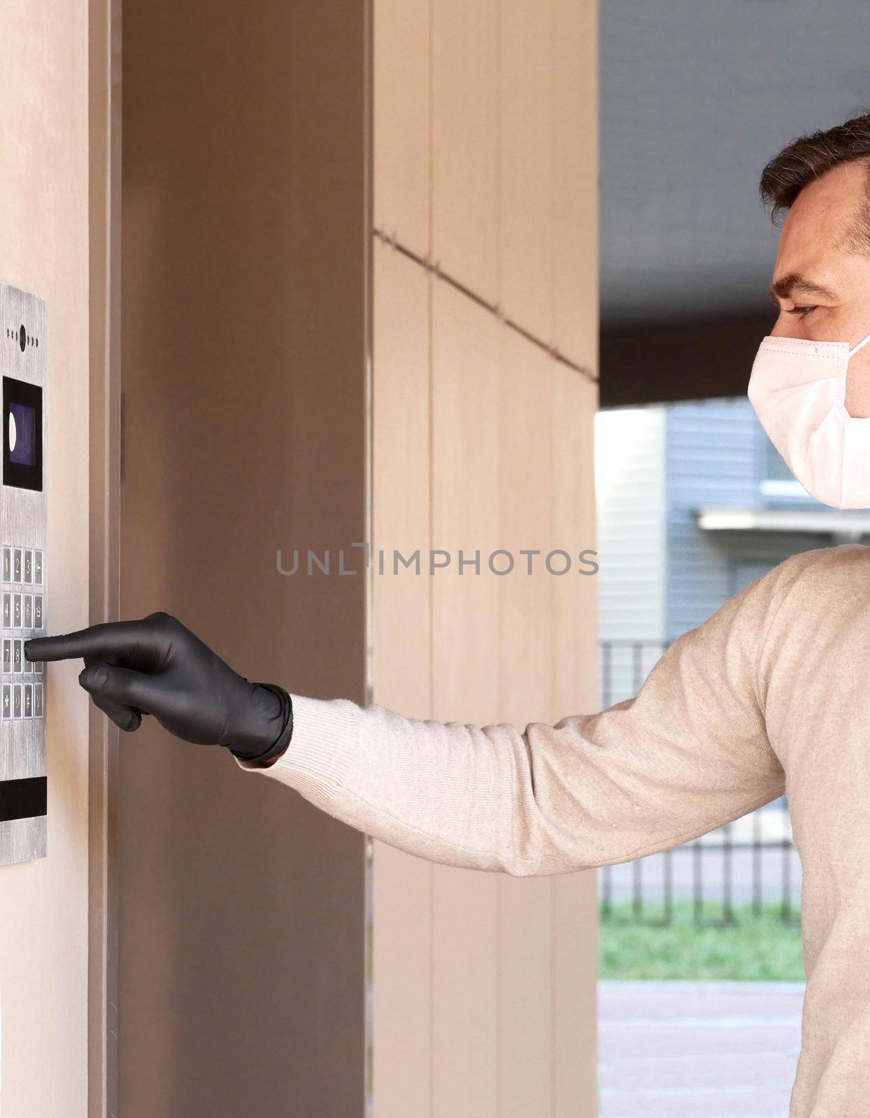 Man in face mask and gloves dials the code on the intercom and going in porch of his apartment. Pandemic covid-19 concept by Jyliana