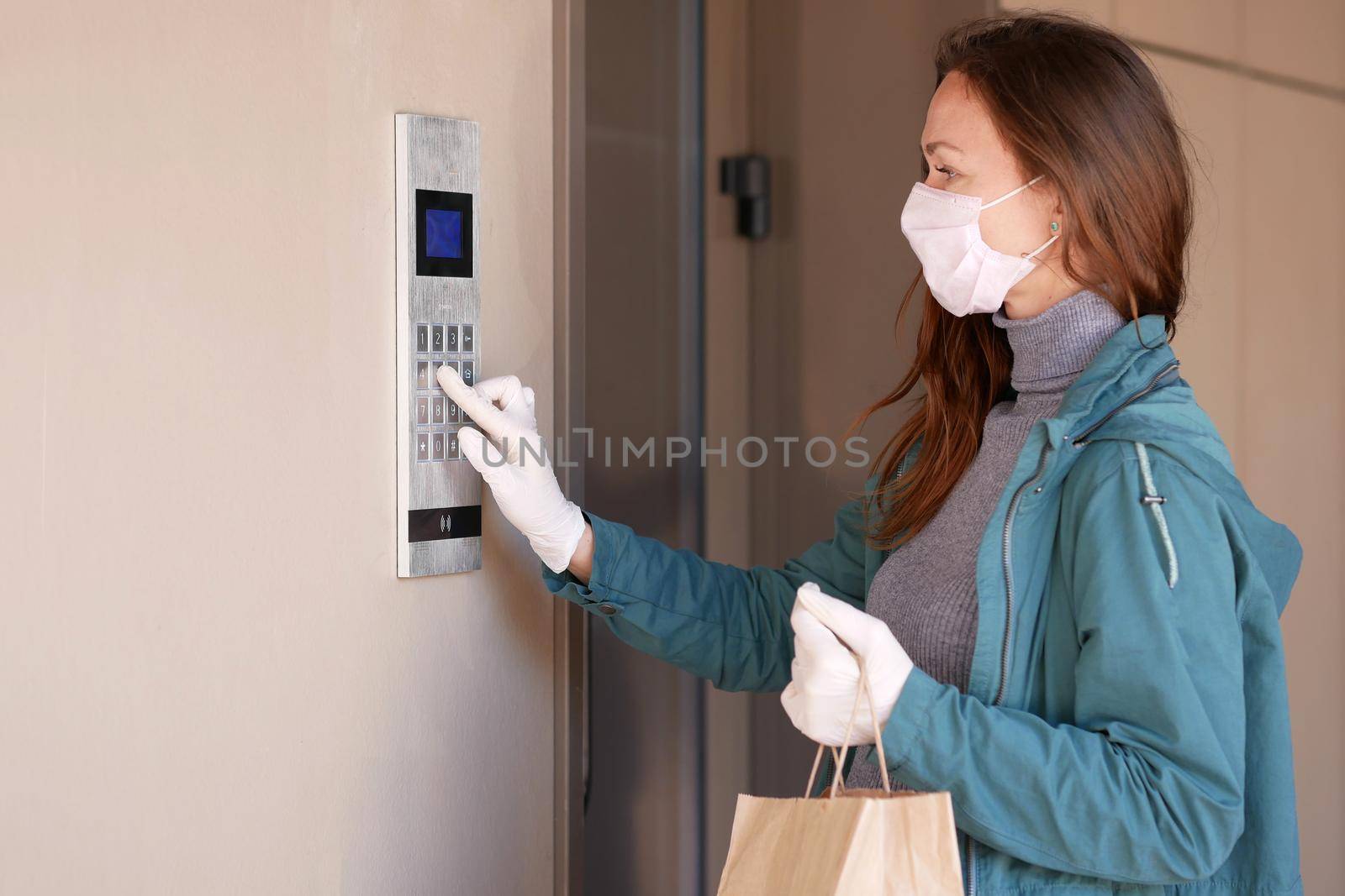 Woman wearing a mask for prevent virus with shopping bags dials the door code Portrait of beautiful happy woman near the door holding shopping bags